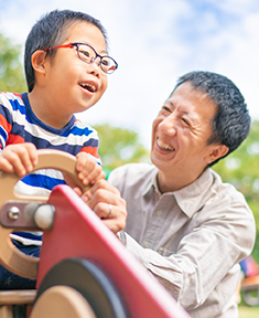 Young Asian boy with Down syndrome enjoying time at an outside public park with his dad