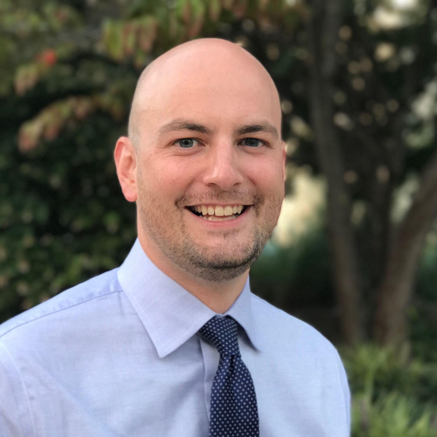 Jake, a white male, wears a dress shirt and tie and smiles at the camera