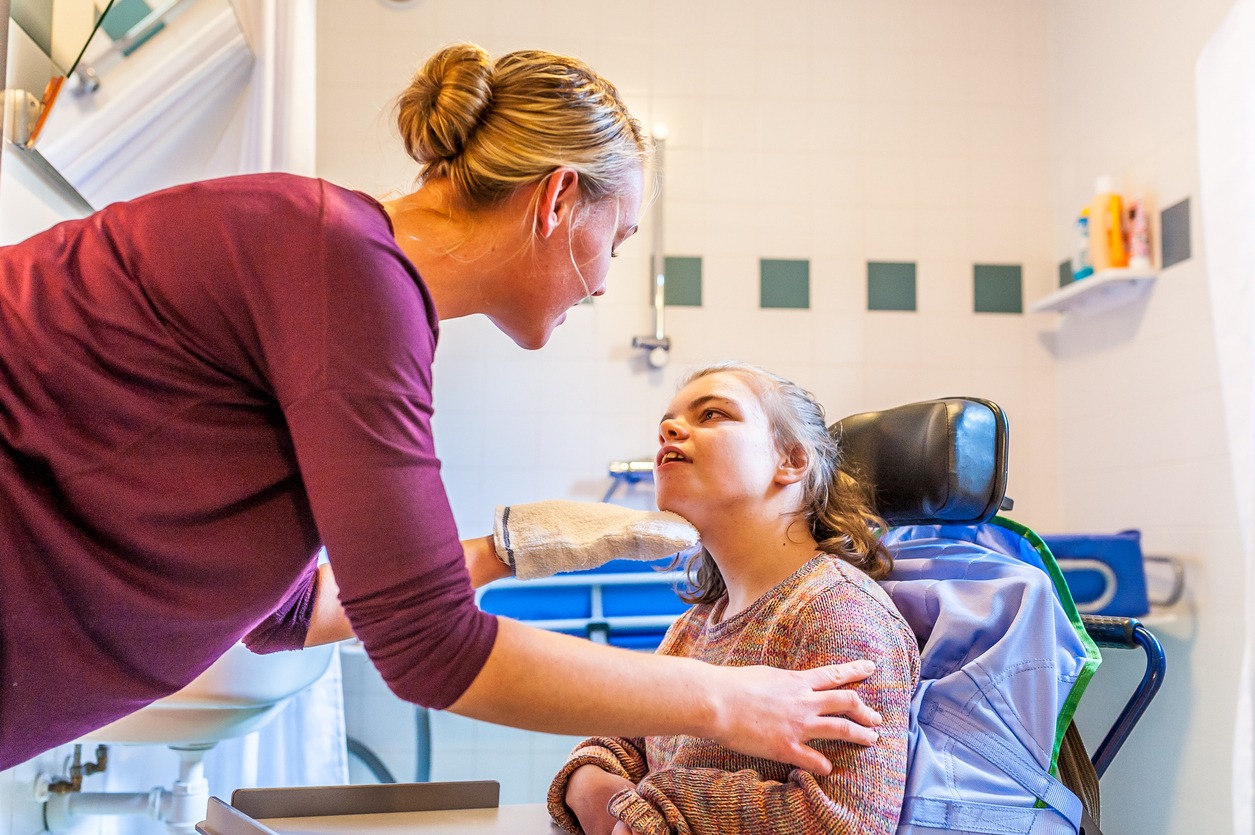 A young girl with disabilities in a wheelchair being cared for by a female nurse.