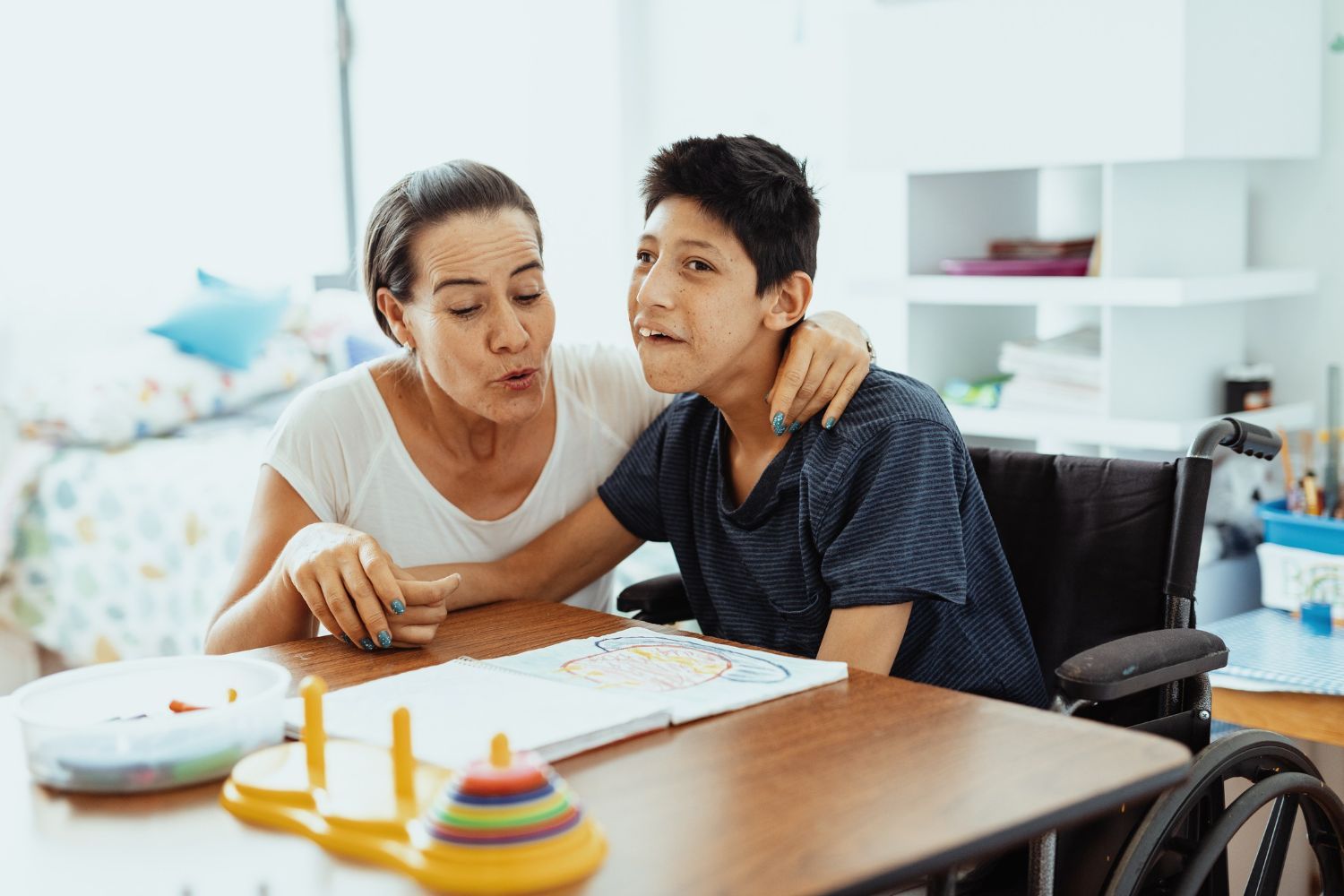 Teen with Cerebral Palsy sits with his mom at a table working on fine motor skills